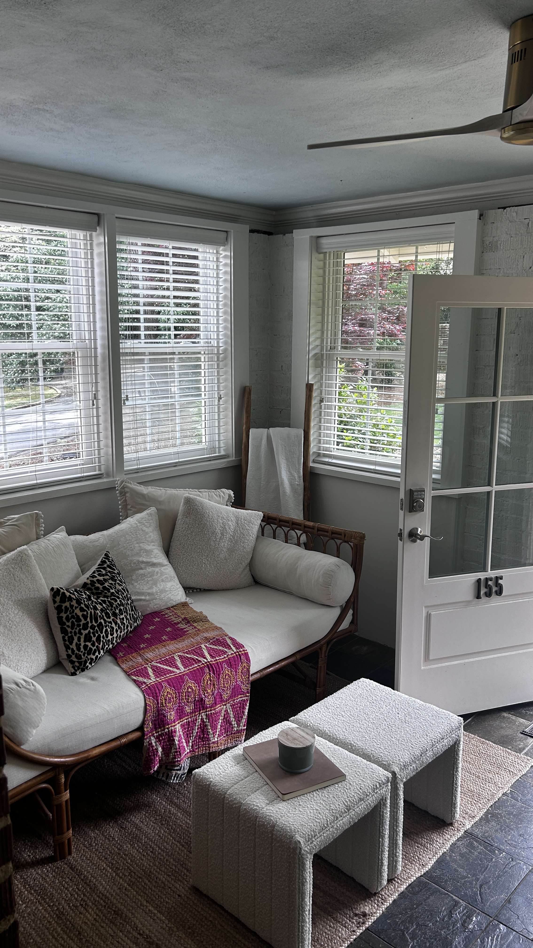 Bright sunroom entry with rattan sofa, layered pillows and '155' painted on the front door