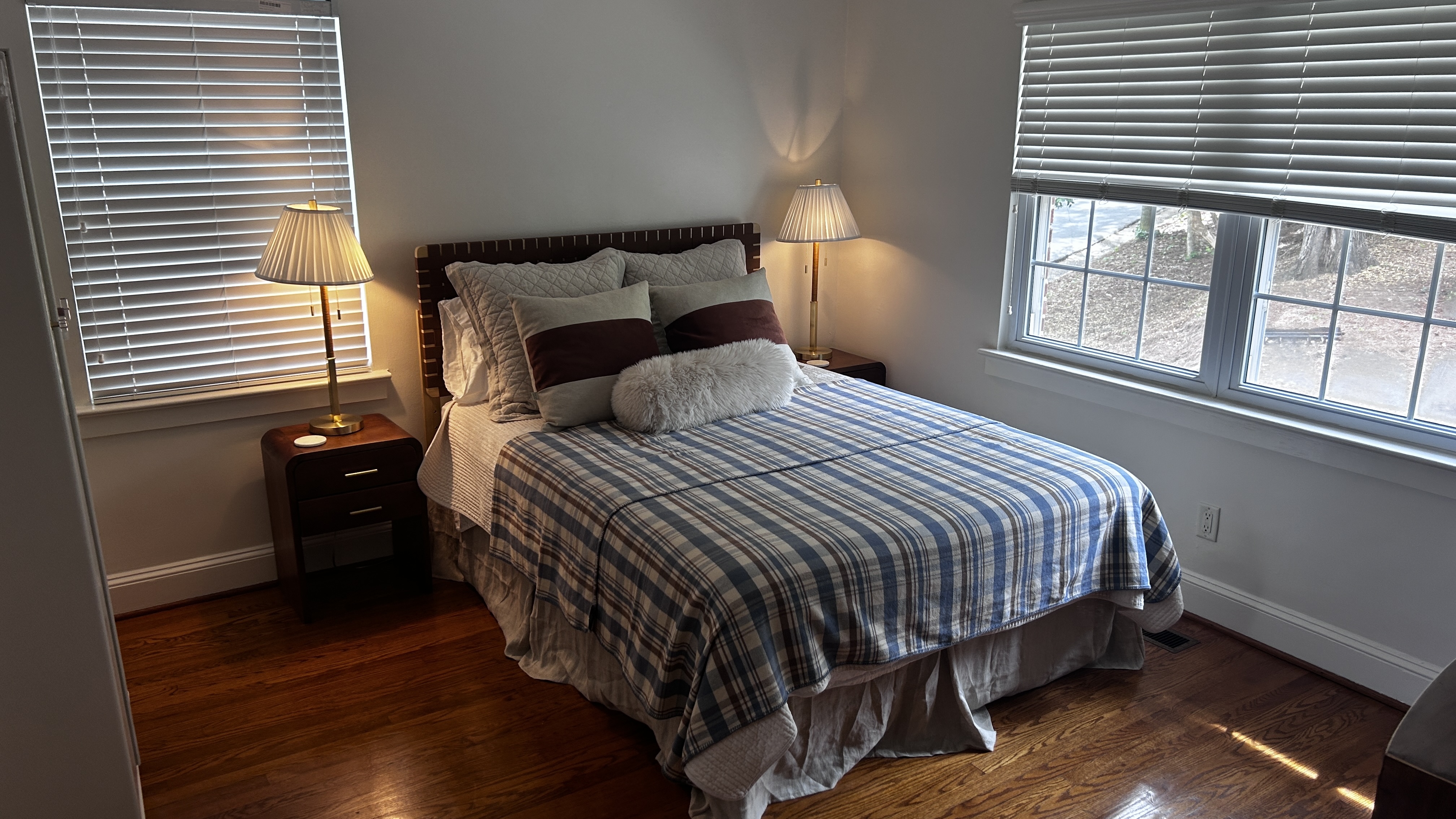 Queen bedroom with blue plaid quilt, brass bedside lamps and hardwood floors