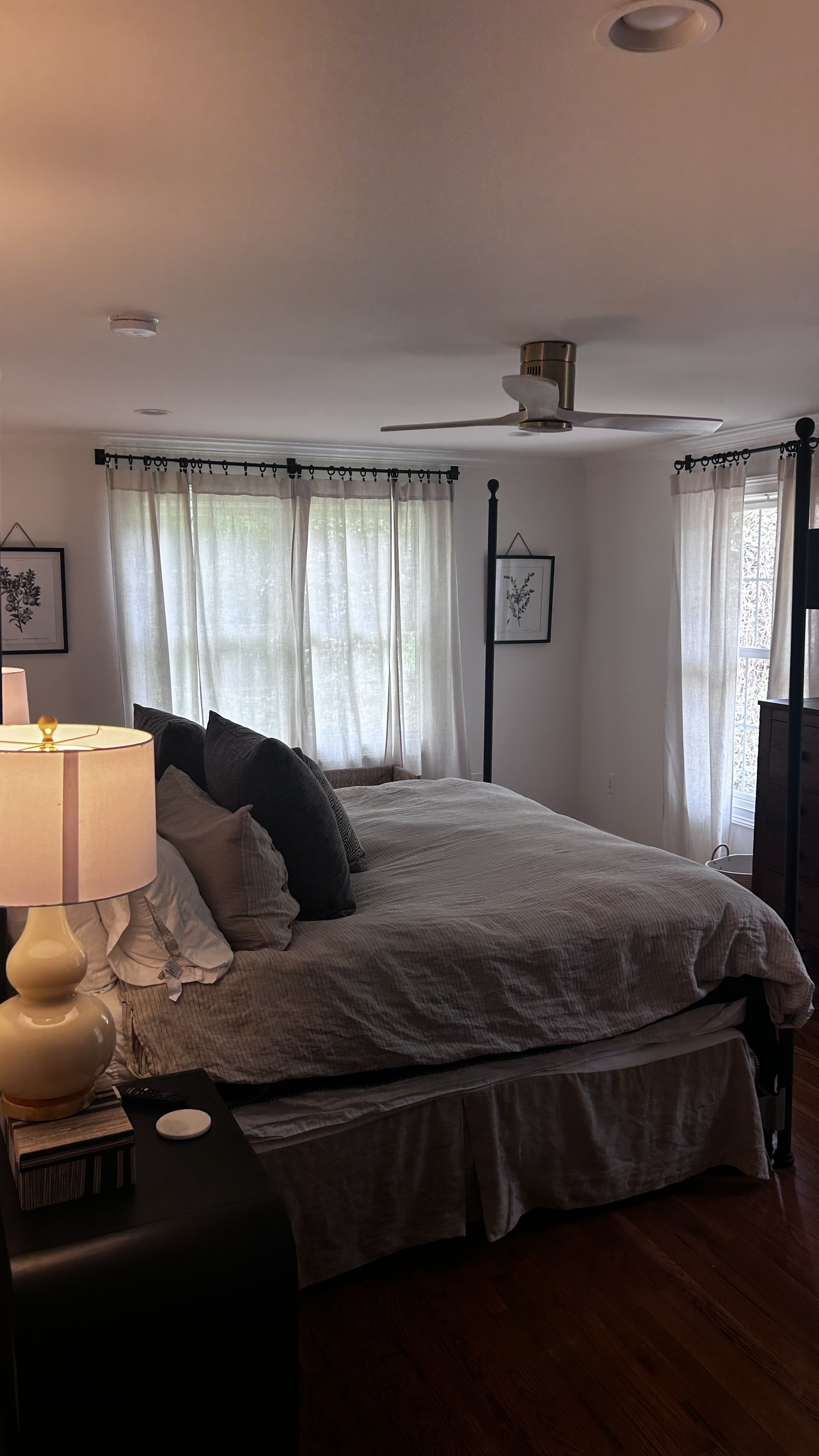 King bedroom wide angle showing sheer linen curtains, ceiling fan and hardwood floors