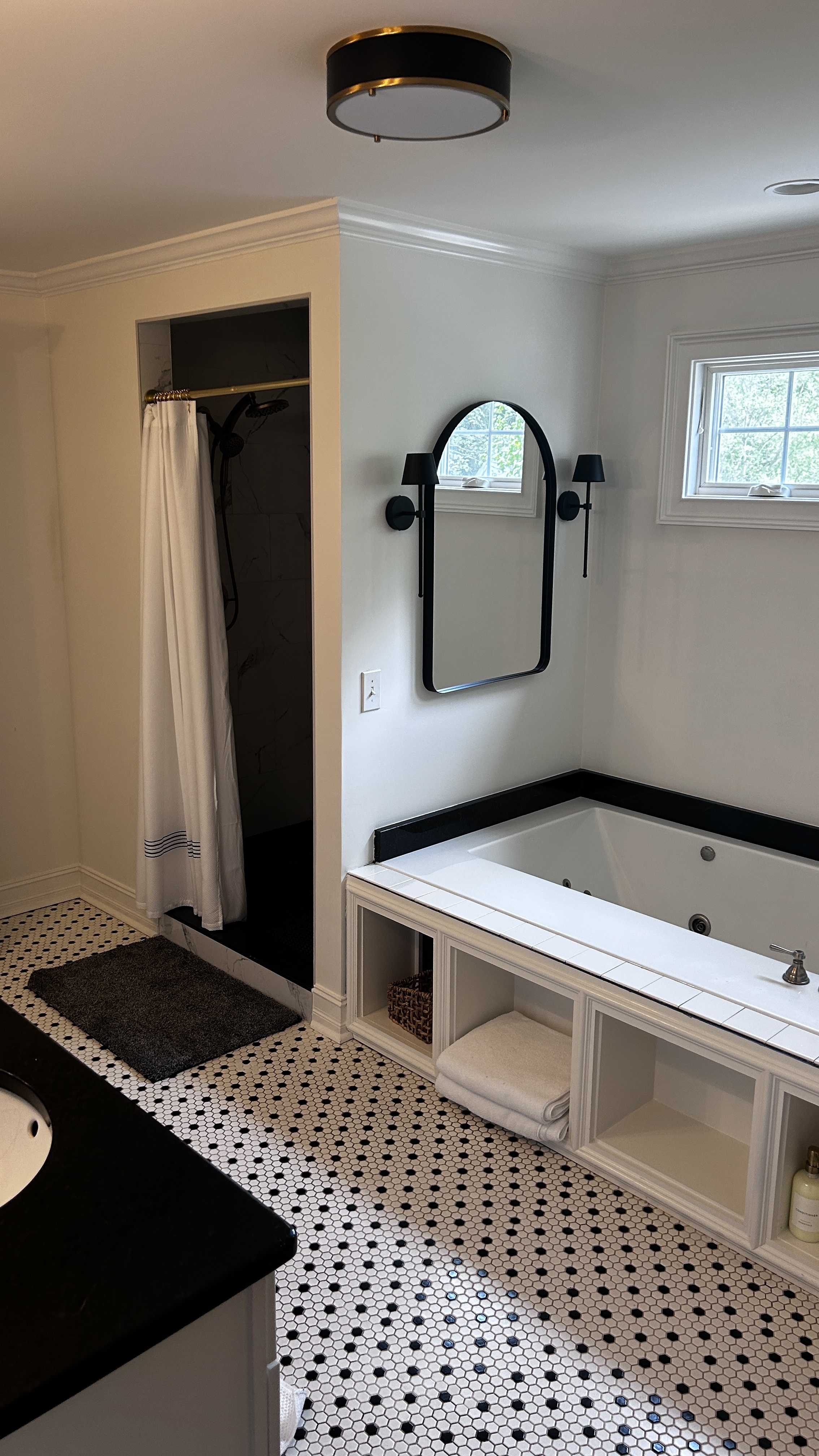 Master bathroom with soaking tub, black-and-white hex tile floor, arched mirror and walk-in shower